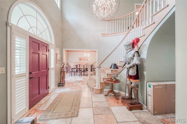 entrance foyer with a chandelier, a high ceiling, plenty of natural light, stairway, and stone tile floors