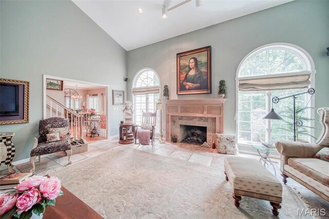 living room with a chandelier, high vaulted ceiling, a high end fireplace, and baseboards