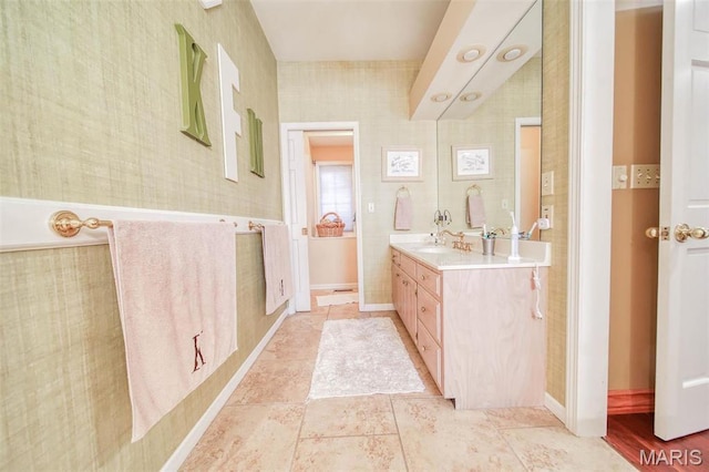 bathroom featuring vanity, wallpapered walls, and baseboards