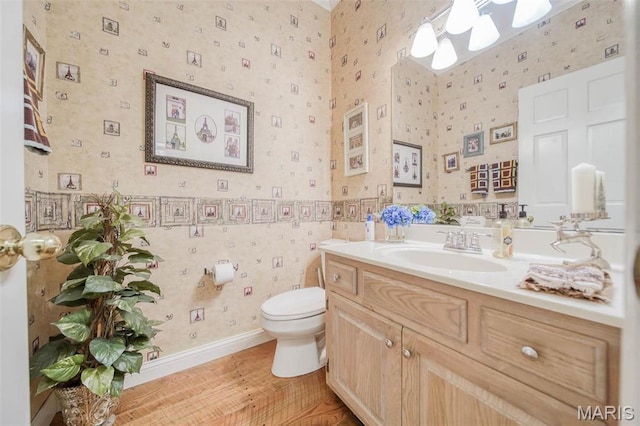 bathroom with wallpapered walls, toilet, vanity, and wood finished floors