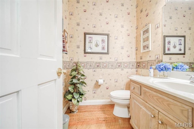 bathroom featuring toilet, wallpapered walls, vanity, baseboards, and wood finished floors