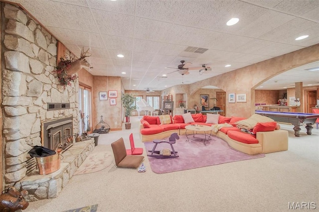 carpeted living room featuring arched walkways, a stone fireplace, recessed lighting, and a ceiling fan
