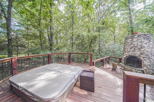 wooden terrace featuring an outdoor stone fireplace, a covered hot tub, and a forest view