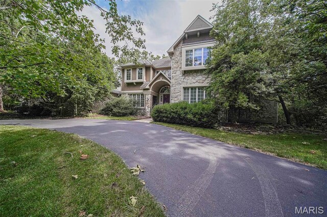 english style home featuring stone siding, asphalt driveway, stucco siding, and a front yard
