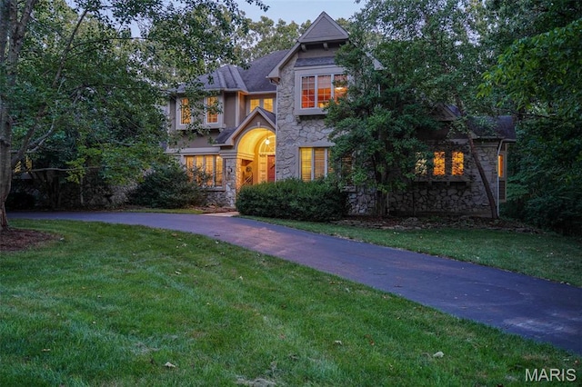 view of front of property featuring stone siding, a front lawn, and asphalt driveway