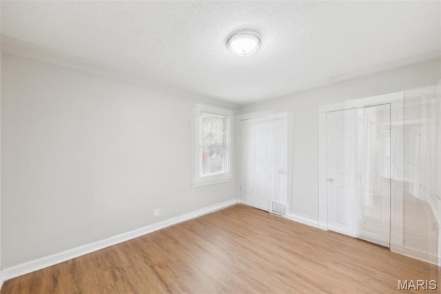 241 Dammert Ave, Saint Louis, MO 63125 - unfurnished bedroom with two closets, light wood-style floors, a textured ceiling, and baseboards