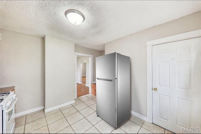 241 Dammert Ave, Saint Louis, MO 63125 - kitchen with freestanding refrigerator, white gas range, light tile patterned floors, baseboards, and a textured ceiling