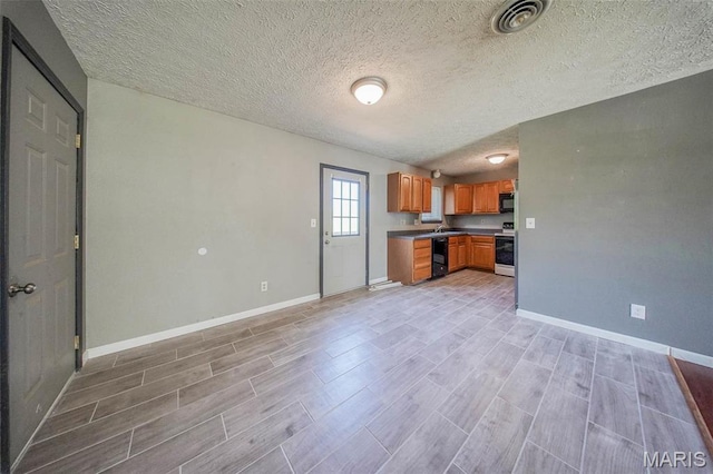 kitchen featuring black appliances, light wood-style flooring, brown cabinetry, baseboards, and a textured ceiling
