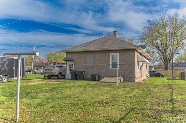 rear view of property with central AC, a lawn, a chimney, stucco siding, and roof with shingles
