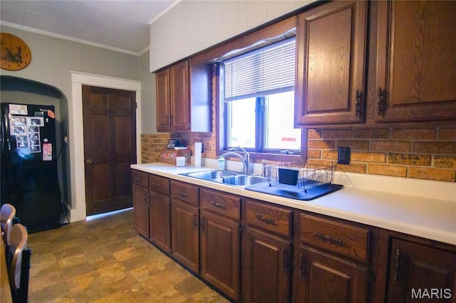 kitchen featuring a sink, freestanding refrigerator, backsplash, light countertops, and crown molding