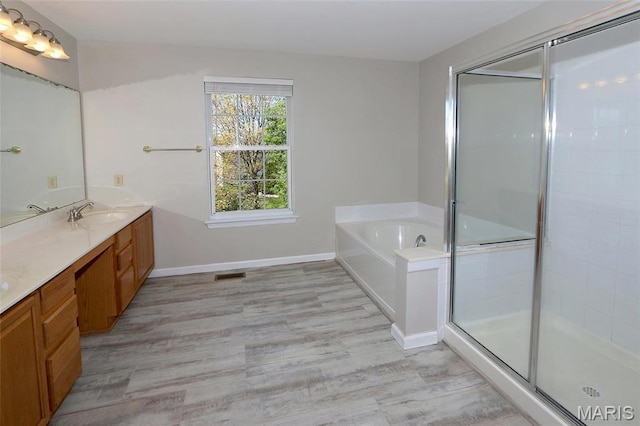 full bathroom featuring a stall shower, vanity, wood finished floors, a bath, and baseboards