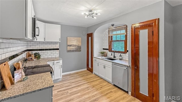 4411 Nelson Dr, Saint Louis, MO 63121 - kitchen with appliances with stainless steel finishes, a sink, arched walkways, backsplash, and light wood-style flooring