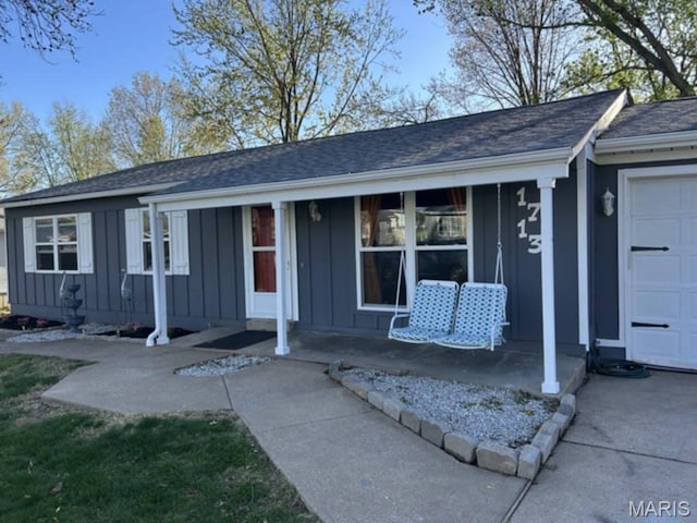 single story home featuring board and batten siding, an attached garage, covered porch, and a shingled roof
