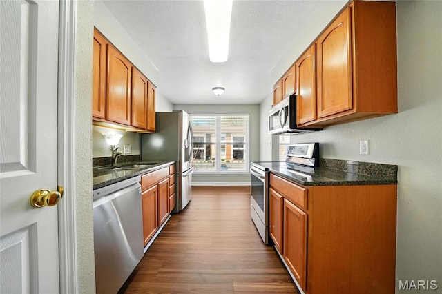 kitchen featuring appliances with stainless steel finishes, a sink, dark wood-type flooring, and brown cabinets