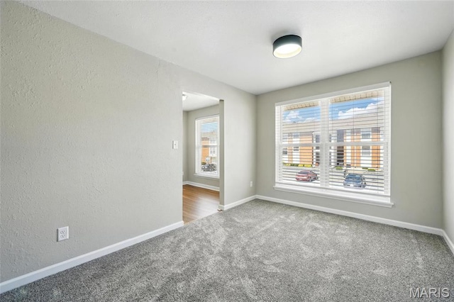 carpeted spare room featuring baseboards and a textured wall