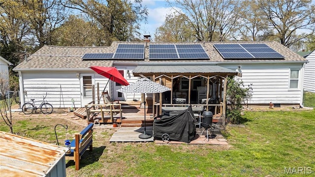 back of house featuring a shingled roof, solar panels, a deck, and a chimney
