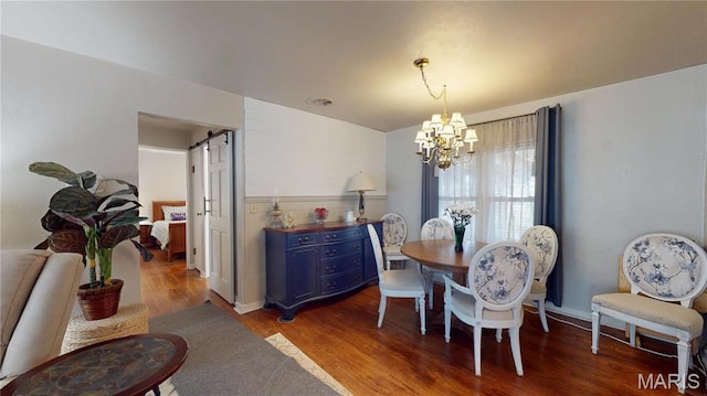 dining area with a chandelier, wood finished floors, and a barn door