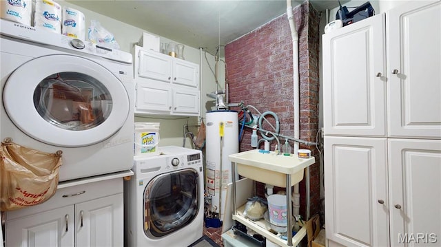 laundry area featuring cabinet space, washer / dryer, water heater, and brick wall