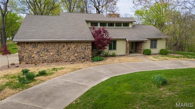 mid-century inspired home with stone siding, a chimney, a shingled roof, and a front yard