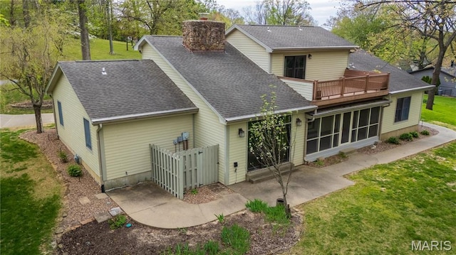 rear view of house featuring a chimney, a shingled roof, a sunroom, a balcony, and a yard