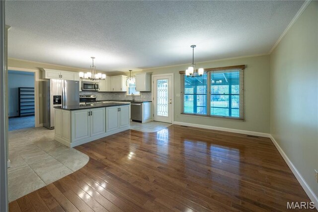 kitchen featuring stainless steel appliances, a chandelier, dark countertops, a textured ceiling, and crown molding