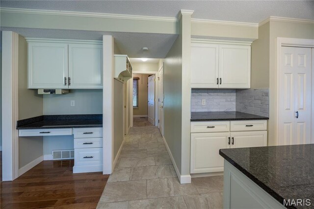 kitchen featuring white cabinetry, decorative backsplash, baseboards, crown molding, and dark stone counters