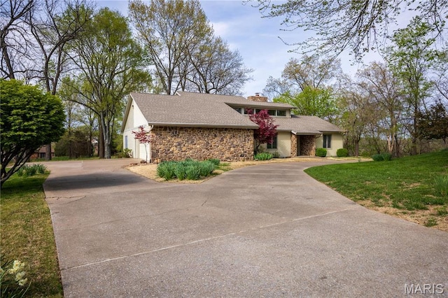 mid-century inspired home featuring stone siding, driveway, a chimney, a garage, and a front yard