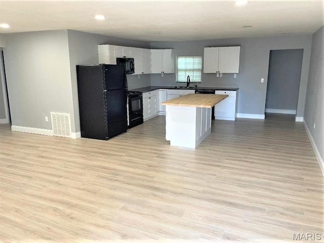 kitchen with black appliances, baseboards, white cabinets, a sink, and a center island
