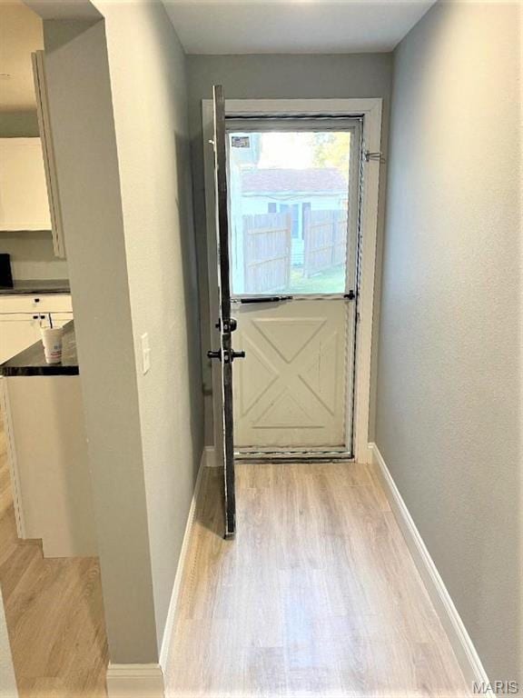 doorway with light wood-style flooring, baseboards, and stairs
