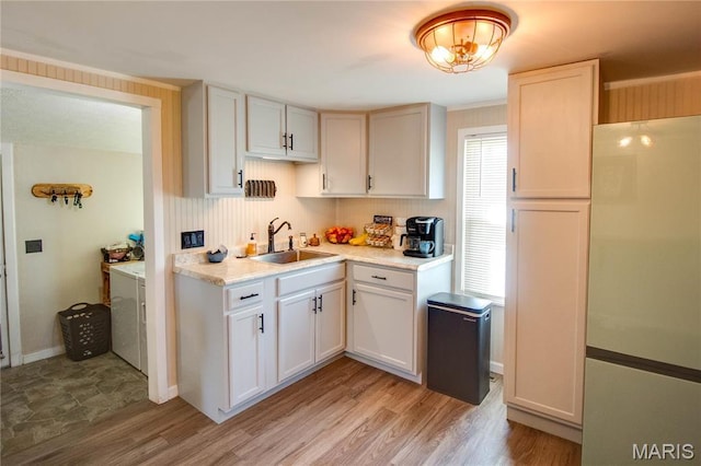 kitchen with freestanding refrigerator, a sink, washer and dryer, light countertops, and light wood-type flooring