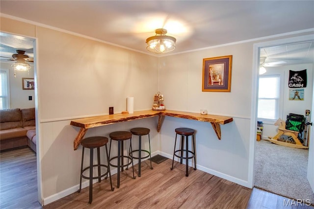 dining space featuring a ceiling fan, wood finished floors, baseboards, crown molding, and a bar
