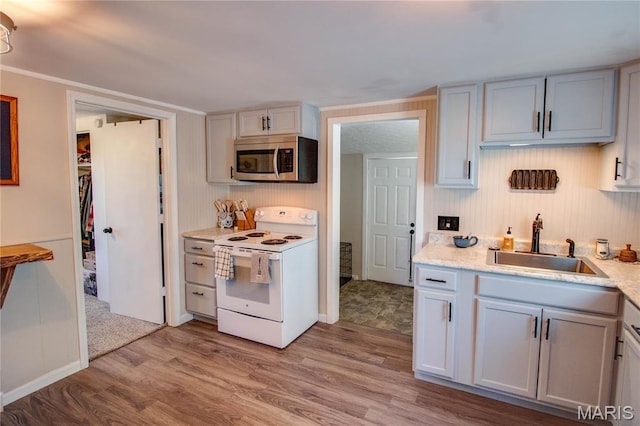 kitchen with white electric range oven, stainless steel microwave, a sink, light wood finished floors, and light countertops
