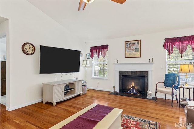 living room with wood finished floors, ceiling fan, vaulted ceiling, a fireplace, and baseboards