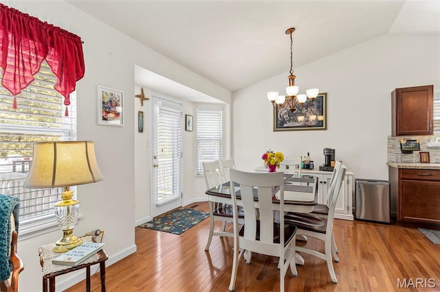 dining area with a chandelier, vaulted ceiling, light wood finished floors, and baseboards