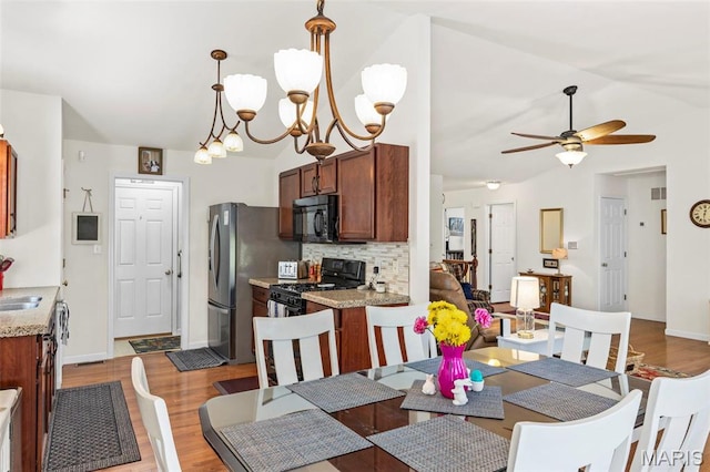 dining area with vaulted ceiling, ceiling fan, wood finished floors, a chandelier, and baseboards