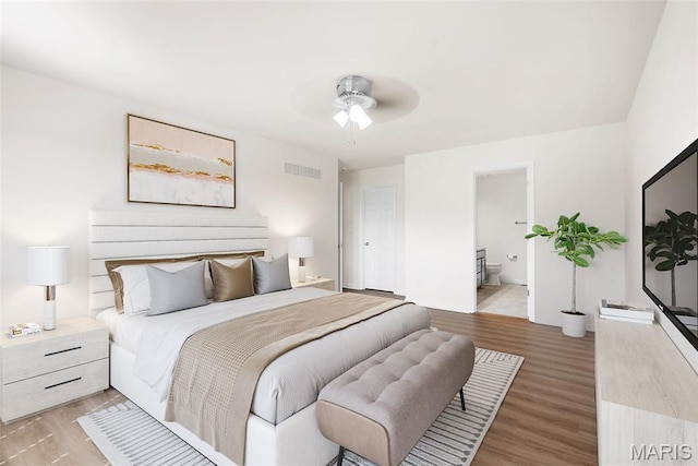 bedroom featuring light wood finished floors, ensuite bath, and a ceiling fan