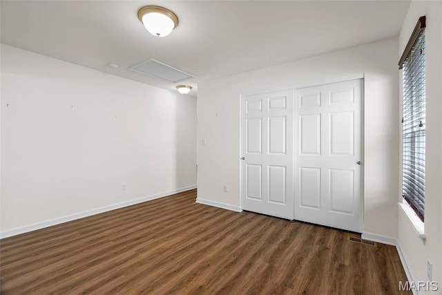 unfurnished bedroom featuring wood finished floors, baseboards, a closet, and attic access