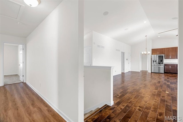 hall with dark wood-style floors, lofted ceiling, baseboards, and a chandelier