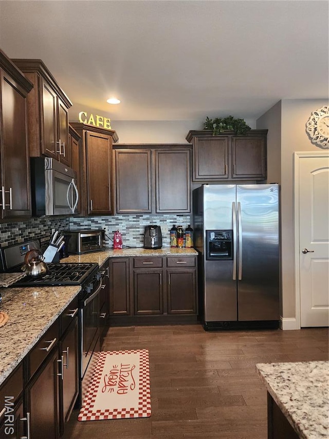 kitchen with appliances with stainless steel finishes, dark brown cabinets, light stone countertops, dark wood-style floors, and tasteful backsplash