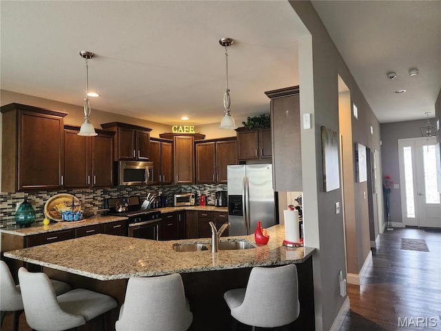 kitchen featuring stainless steel appliances, a sink, baseboards, a peninsula, and dark brown cabinets