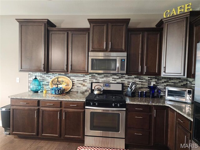 kitchen featuring appliances with stainless steel finishes, dark brown cabinets, decorative backsplash, and light stone countertops