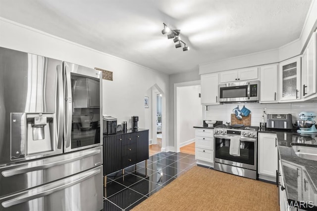 3644 Eminence Blvd, Saint Louis, MO 63114 - kitchen featuring appliances with stainless steel finishes, dark countertops, decorative backsplash, white cabinetry, and arched walkways