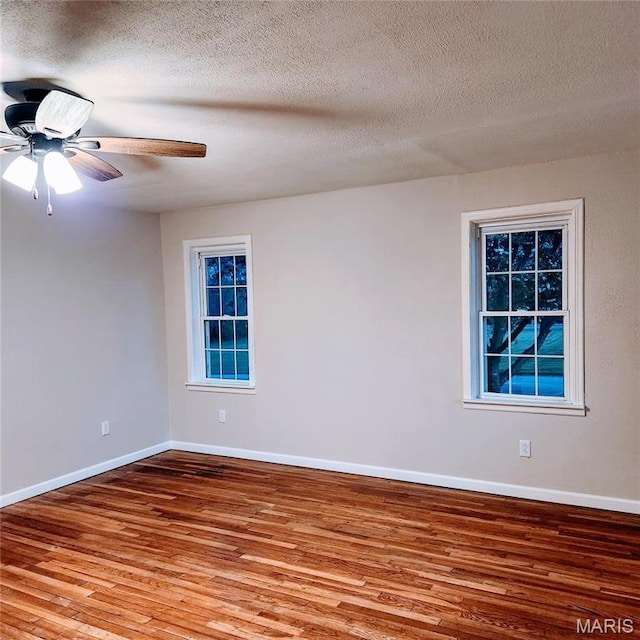 empty room with wood finished floors, baseboards, a ceiling fan, and a textured ceiling