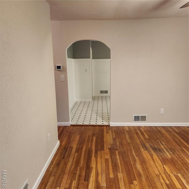 empty room with arched walkways, hardwood / wood-style flooring, and baseboards