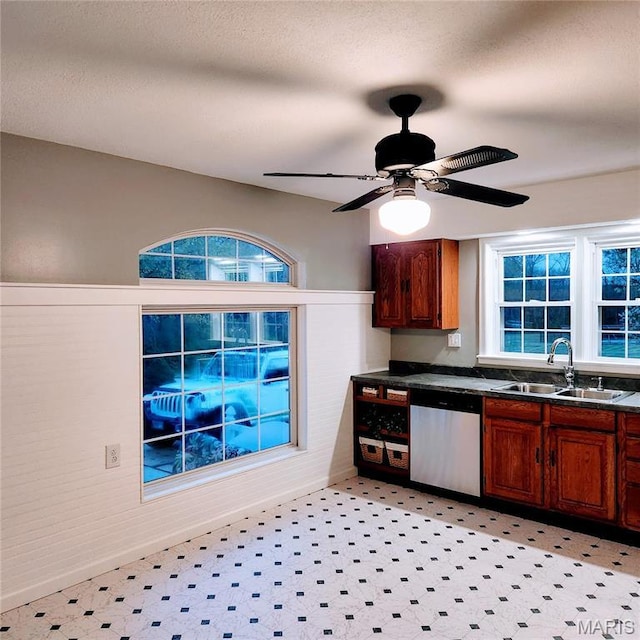 kitchen featuring dishwasher, a sink, dark countertops, ceiling fan, and light flooring