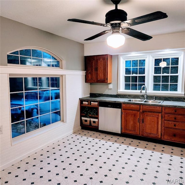 kitchen featuring a sink, dishwasher, dark countertops, light flooring, and brown cabinets