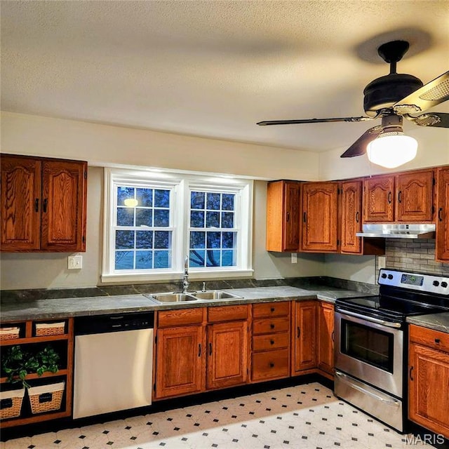 kitchen featuring stainless steel appliances, under cabinet range hood, a sink, dark countertops, and brown cabinets