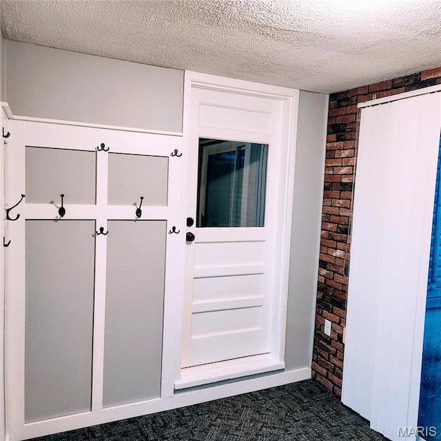 mudroom with brick wall, a textured ceiling, and dark carpet