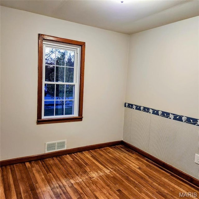 spare room featuring hardwood / wood-style floors, baseboards, and a wainscoted wall