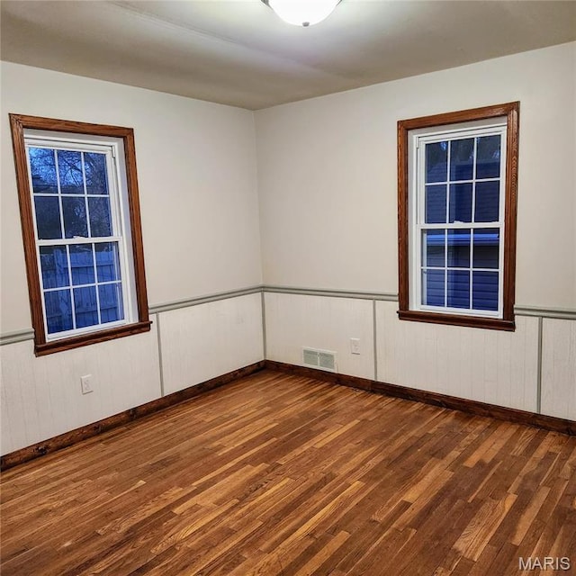 empty room with wood finished floors, baseboards, and wainscoting
